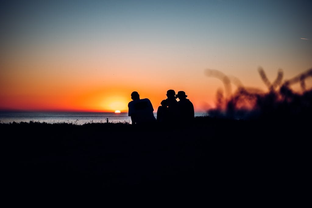 Silhouetted festivalgoers watch the sun go down at Fistral Beach during Boardmasters Festival at golden hour.