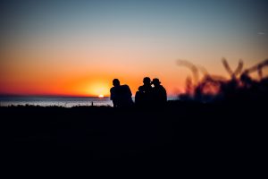 Silhouetted festivalgoers watch the sun go down at Fistral Beach during Boardmasters Festival at golden hour.