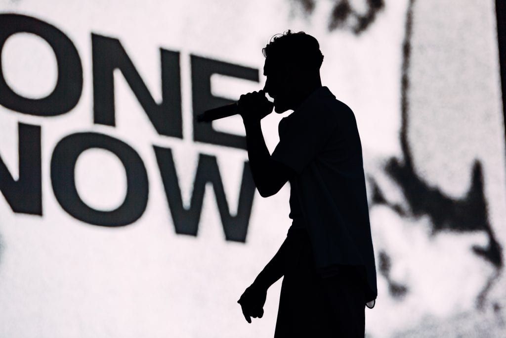 Harvey Kirkby of Everyone You Know silhouetted against a bright backdrop during a live performance at Boardmasters Festival.