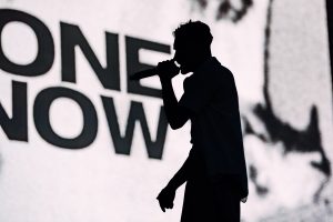 Harvey Kirkby of Everyone You Know silhouetted against a bright backdrop during a live performance at Boardmasters Festival.