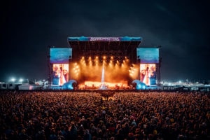 Wide-angle shot of Florence and the Machine's live performance at Boardmasters Festival, featuring a stage bathed in hues of blue and orange light, with a sea of spectators under the night sky.